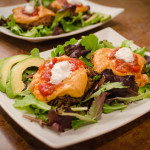 Black bean burger on a plate of greens with cheese sauce, salsa and sour cream