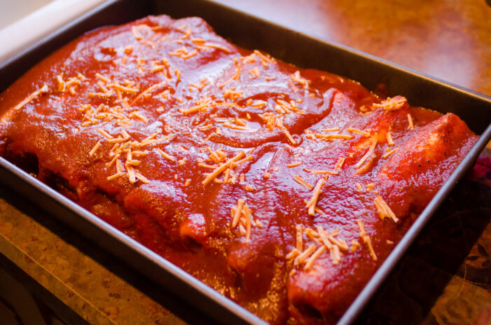 veggie enchiladas assembled, topped with sauce and shreds, and ready for the oven.