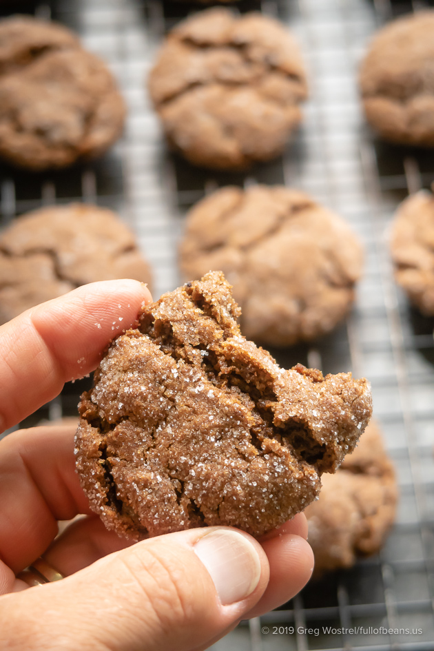 Vegan Molasses Cookies held close to camera with an out of focus rack of cookies in the background
