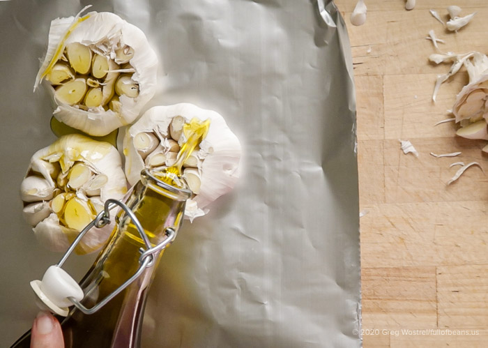 pouring olive oil on the cut garlic heads