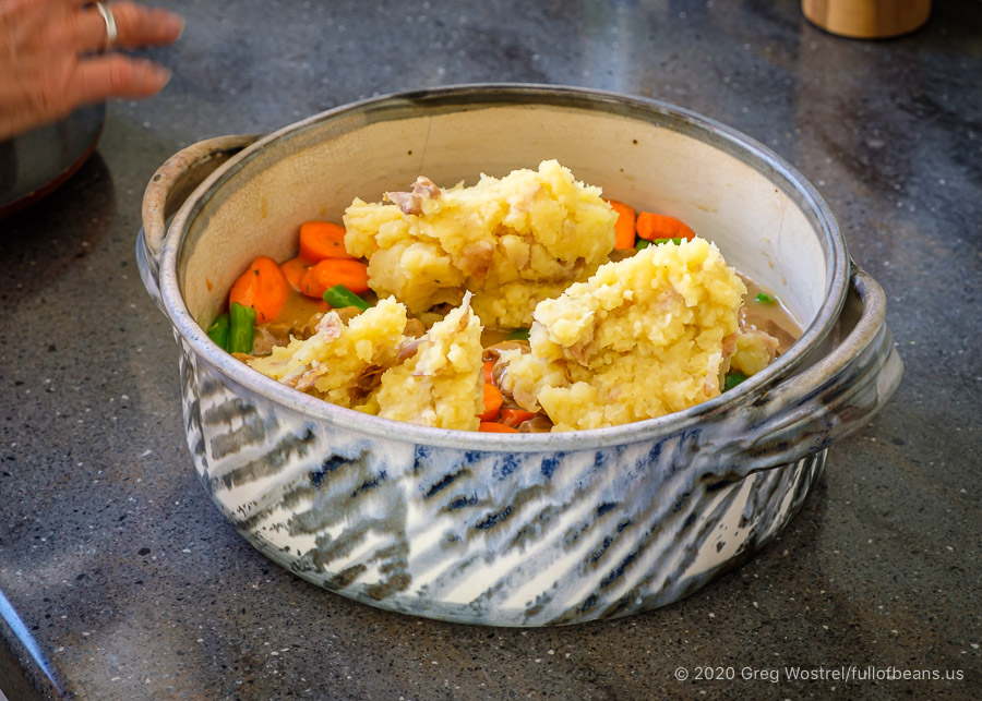 preparing vegan Shepherd's pie: mashed potatoes added to the dish with veggies and seitan