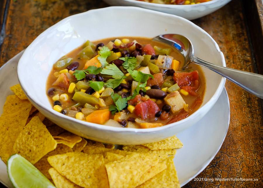 A bowl of Vegan Mexican Soup on a plate with corn chips and a lime wedge
